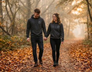 A stylish couple holding hands and wearing premium matching couples halloween hoodies in a foggy autumn park